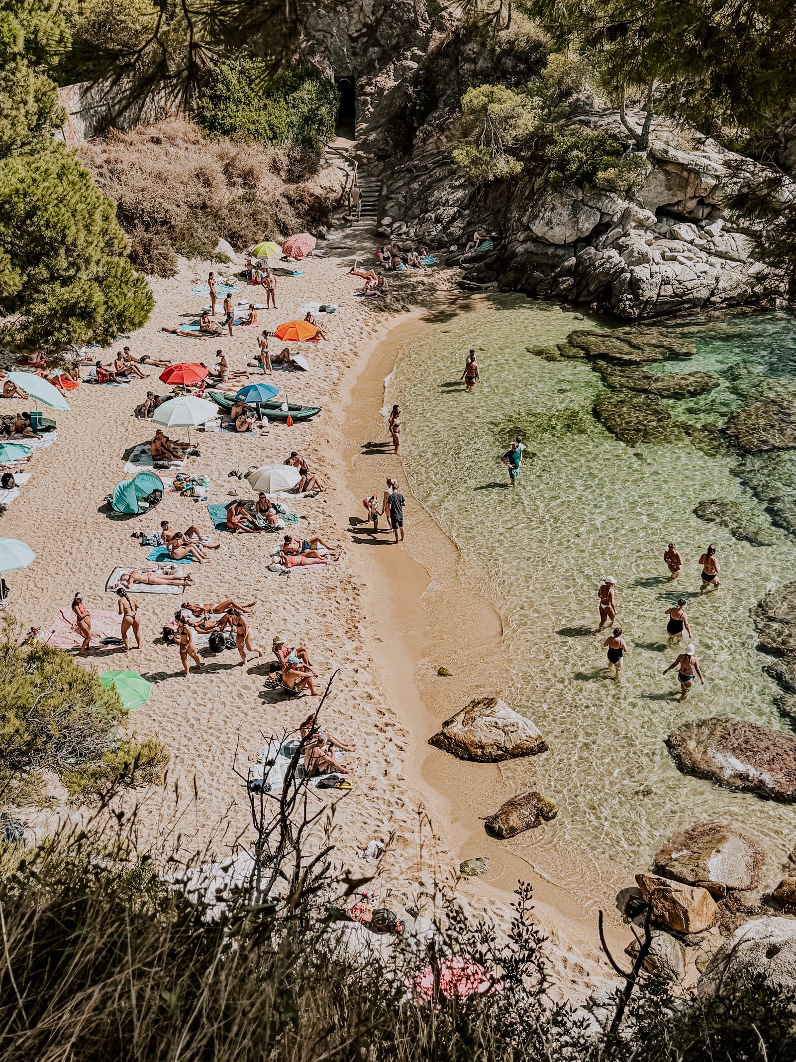 A lively Costa Brava cove with beach umbrellas and swimmers in clear turquoise water